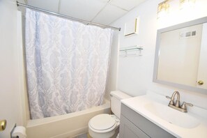 A bathroom with a toilet, a bathtub, a shower curtain, a sink, and a mirror. - Ocean Trail 102 2 Br condo by RedAwning (Ocean City)