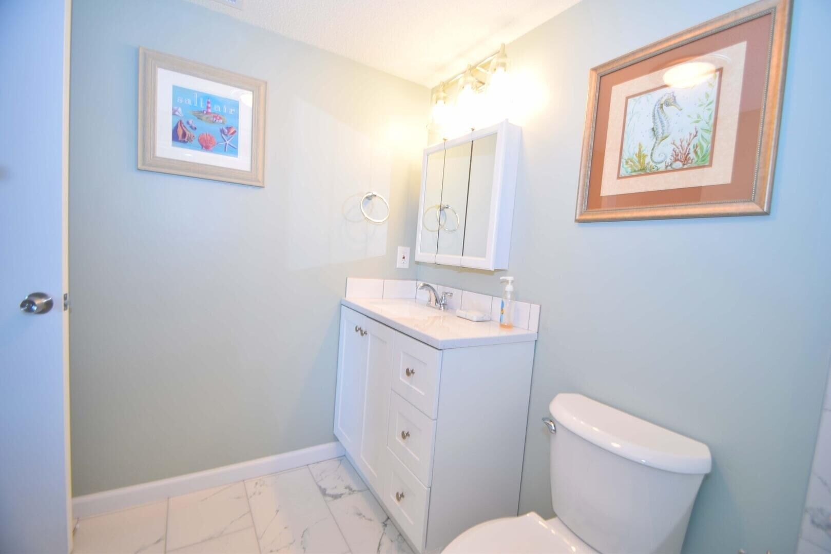 A bathroom with a toilet, a sink with a mirror above it, and two framed pictures on the walls.