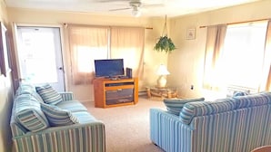 A living room with striped sofas, a television on a wooden cabinet, a hanging plant, and a lamp on a glass table. - Severn I 208 3 Br condo by RedAwning (Ocean City)
