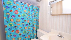 A bathroom with a shower curtain featuring colorful fish patterns, a white toilet, and a sink with a mirror above it. - Shore Lea 102 1 Br condo by RedAwning (Ocean City)