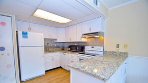 A compact kitchen with white cabinets, a refrigerator, a microwave, an oven, and granite countertops. - Shore Lea 102 1 Br condo by RedAwning (Ocean City)