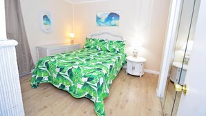 A bedroom with a bed, a bedside table, a lamp, a radiator, and a mirror. - Shore Lea 102 1 Br condo by RedAwning (Ocean City)