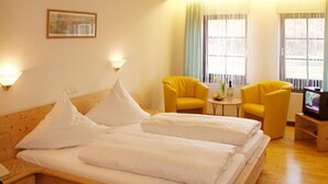 Une chambre d’hôtel avec un lit en bois, deux fauteuils jaunes, une petite table avec une lampe et un téléviseur posé sur un meuble en bois.