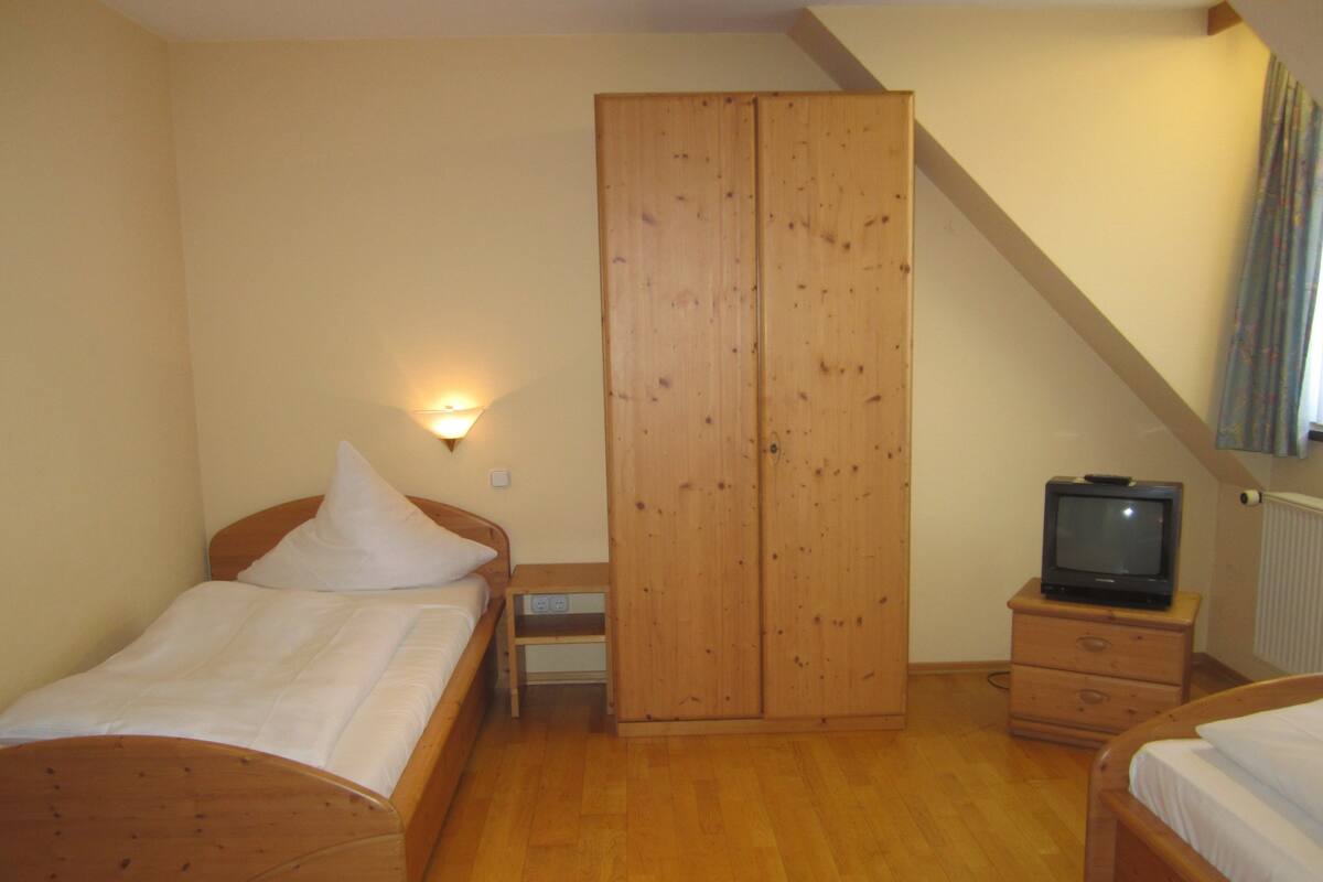Ein Schlafzimmer mit zwei Holzbetten, einem Holzschrank, einem Nachttisch, einem Fernseher und einer Wandleuchte.