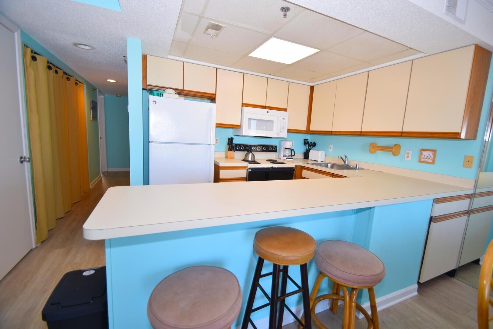 A compact kitchen with a central island, a microwave, a stove, and bar stools.
