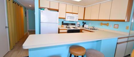 A compact kitchen with a central island, a microwave, a stove, and bar stools.