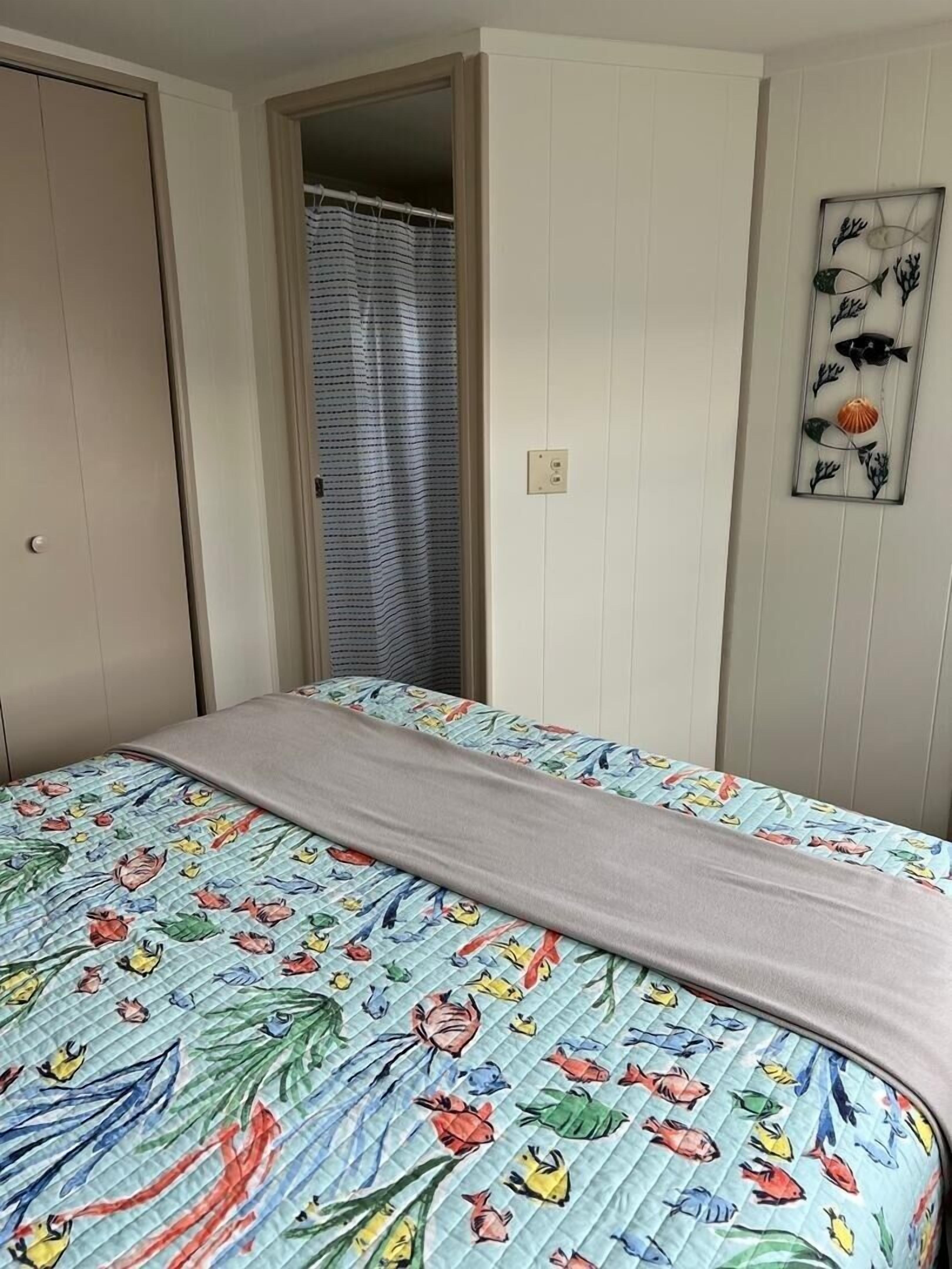 A bedroom with a bed featuring a floral and fish pattern bedspread, a neutral-colored blanket, a wooden door, and a wall-mounted fish decoration.