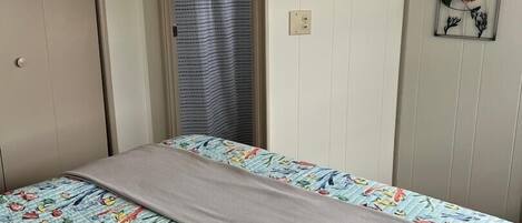 A bedroom with a bed featuring a floral and fish pattern bedspread, a neutral-colored blanket, a wooden door, and a wall-mounted fish decoration.