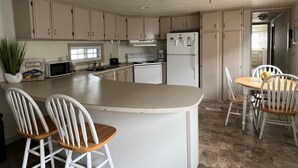 A kitchen with a central island, white cabinets, a refrigerator, a microwave, and a dining area with a table and chairs. - Montego Bay - Peachtree Road 122 3 Bedroom Home by RedAwning (Ocean City)