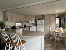 Una cocina con una isla central, armarios blancos, un refrigerador, un microondas y un comedor con mesa y sillas.