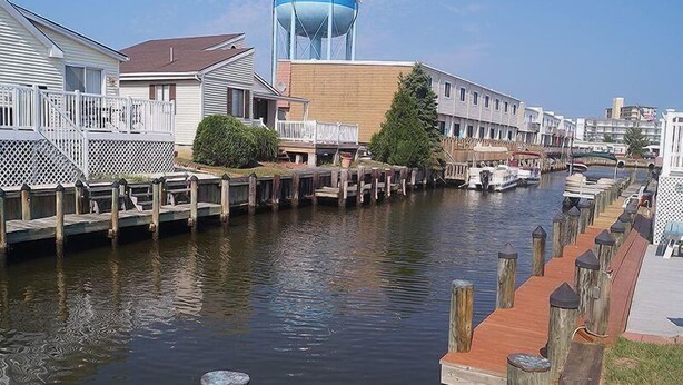 A canal with wooden walkways and boats, surrounded by residential buildings and a water tower. - Montego Bay - Peachtree Road 122 3 Bedroom Home by RedAwning (Ocean City)