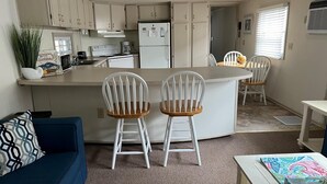 A compact kitchen with a central island, white cabinets, and a dining area with two white chairs. - Montego Bay - Peachtree Road 122 3 Bedroom Home by RedAwning (Ocean City)