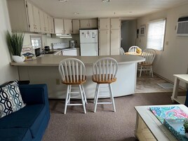 Una cocina compacta con una isla central, armarios blancos y un comedor con dos sillas blancas.