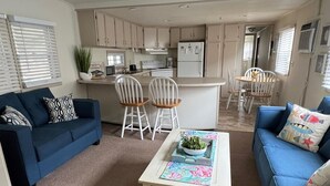 A compact living space with a kitchenette, a blue sofa, a coffee table, and a dining area with white chairs. - Montego Bay - Peachtree Road 122 3 Bedroom Home by RedAwning (Ocean City)