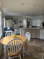 Cocina compacta con muebles blancos, una mesa de madera con cuatro sillas y una pequeña encimera con lavamanos.