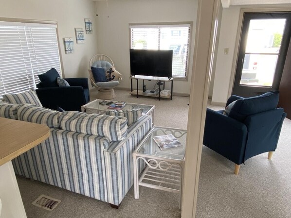 A living room with a striped sofa, a chair with a cushion, a coffee table, and a television on a stand. - Montego Bay - South Ocean Drive 203 3 Bedroom Home by RedAwning (Ocean City)