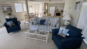 A living room with a striped sofa, two armchairs, a coffee table, and a dining area with a kitchen in the background. - Montego Bay - South Ocean Drive 203 3 Bedroom Home by RedAwning (Ocean City)