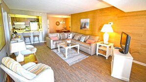 A living room with a sofa, coffee table, and TV stand. There is a dining area with chairs and a table. - Braemar 503N 2 Br condo by RedAwning (Ocean City)