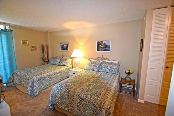 A bedroom with two beds, a bedside table with a lamp, a vase with flowers, and two framed pictures on the wall. - Braemar 503N 2 Br condo by RedAwning (Ocean City)