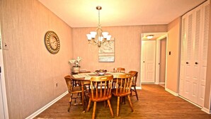 A dining room with a chandelier, wooden chairs, a clock, and a door leading to a closet. - Braemar 503N 2 Br condo by RedAwning (Ocean City)