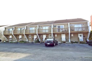 A multi-story motel with balconies, a parking lot, and a black car parked in front. - Crab Harbour 4 3 Bedroom Townhouse by RedAwning (Ocean City)