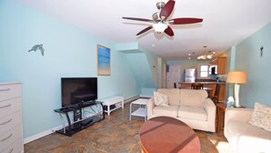 A living room with a TV, sofa, coffee table, and ceiling fan. - Crab Harbour 4 3 Bedroom Townhouse by RedAwning (Ocean City)