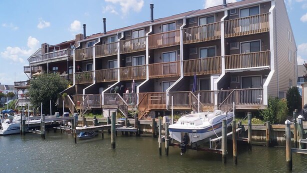 A multi-story building with balconies, docked boats, and a clear sky. - Crab Harbour 4 3 Bedroom Townhouse by RedAwning (Ocean City)