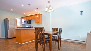 A modern kitchen with wooden cabinets, a stainless steel refrigerator, a microwave, and a dining table with chairs. - Crab Harbour 4 3 Bedroom Townhouse by RedAwning (Ocean City)