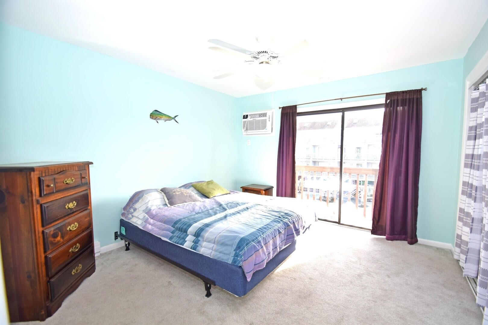 A bedroom with a bed, a dresser, a ceiling fan, and a window with curtains.