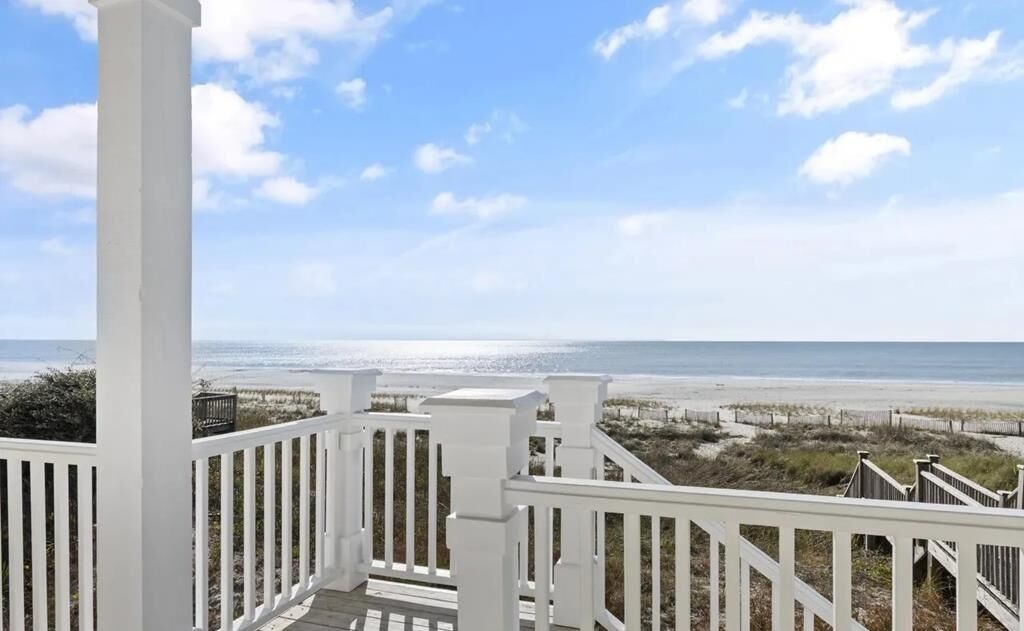 A white wooden deck with a view of the beach and ocean.