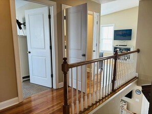 A staircase with a wooden handrail and white balusters, leading to a landing with a television and a bookshelf.