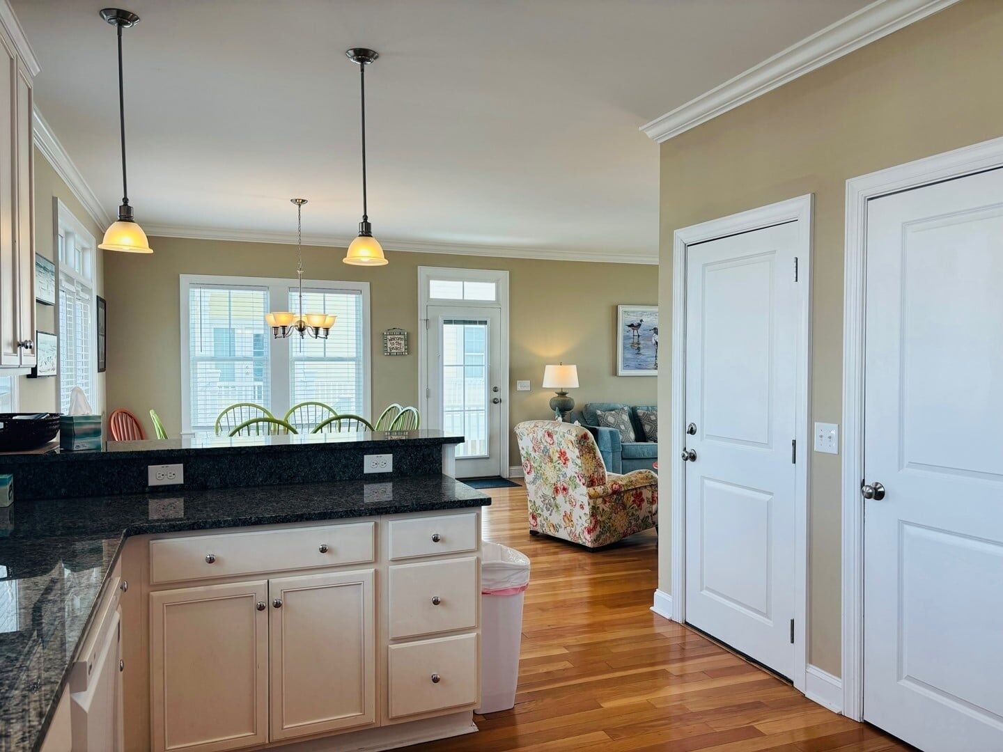 A kitchen with a marble countertop, white cabinets, and pendant lights.