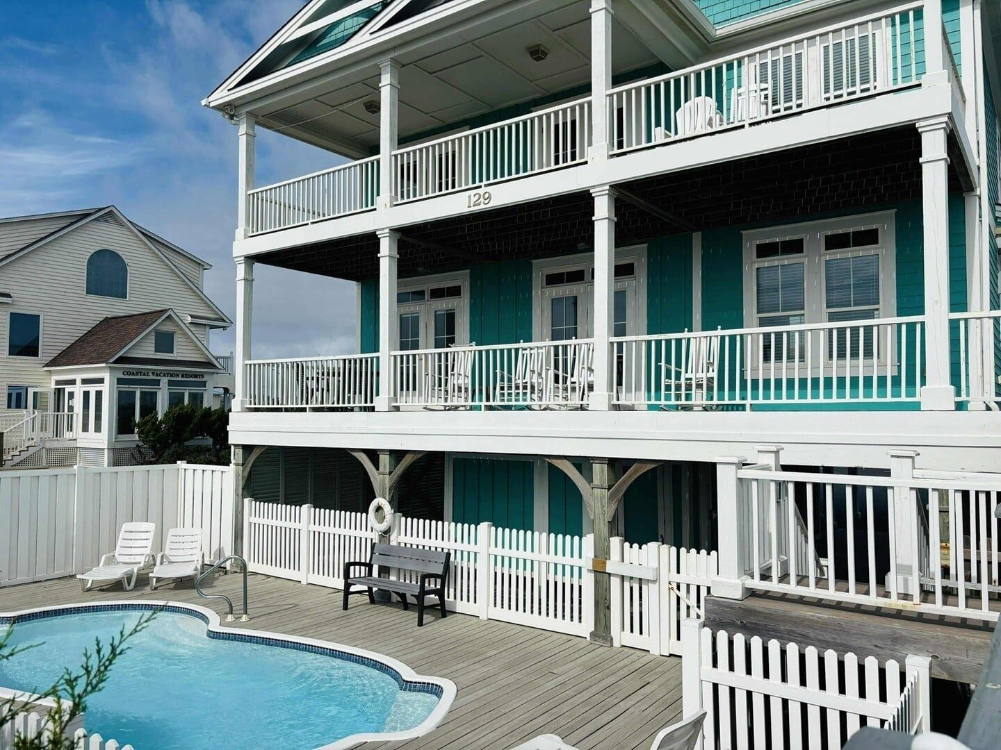 A two-story building with a balcony, a pool, and a white picket fence.