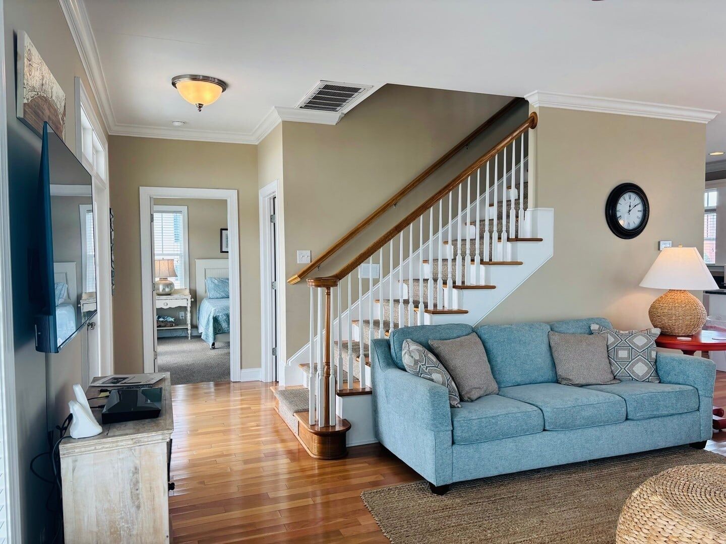 A living room with a blue sofa, wooden staircase, and a flat-screen TV mounted on the wall.