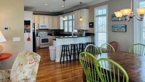 A kitchen with white cabinets, a central island with stools, and a dining area with a wooden table and green chairs.