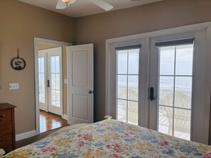 A bedroom with a bed, a dresser, and a view of the beach through a door. - 1 Fine Day 4 Bedroom Home by RedAwning (Supply)