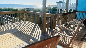 A wooden deck with a view of the ocean and a white building in the background. - 3/4 Time - 4 Br Home (Supply)