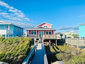 A coastal house with a wooden deck, a small porch, and a clear view of the ocean.
