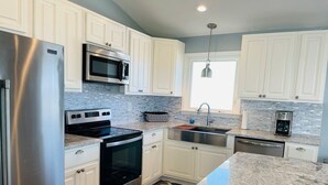 A modern kitchen with white cabinets, stainless steel appliances, a granite countertop, and a wooden floor. - 3/4 Time - 4 Br Home (Supply)