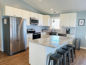 A modern kitchen with white cabinets, stainless steel appliances, a granite countertop, and a bar stool seating area. - 3/4 Time - 4 Br Home (Supply)