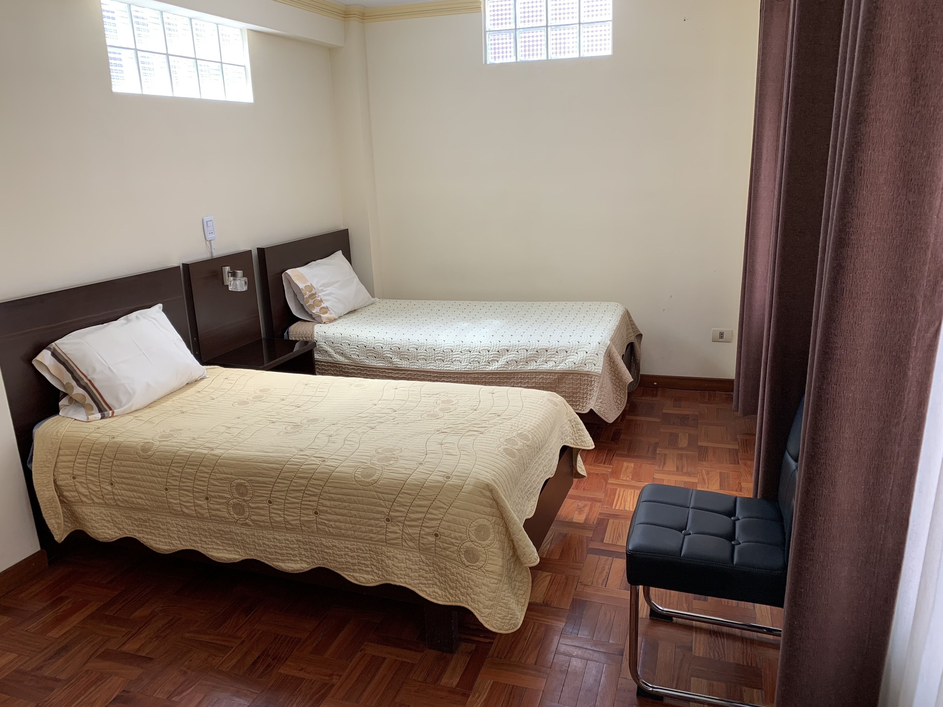 A room with two beds, wooden flooring, and a small black chair.