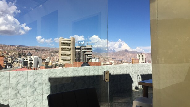 Un paisaje urbano con cielo despejado, un edificio con el letrero 'tigo' y una pared de azulejos.