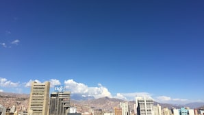 Un paisaje urbano con edificios altos, incluyendo un llamativo letrero de 'tigo', bajo un cielo azul despejado.
