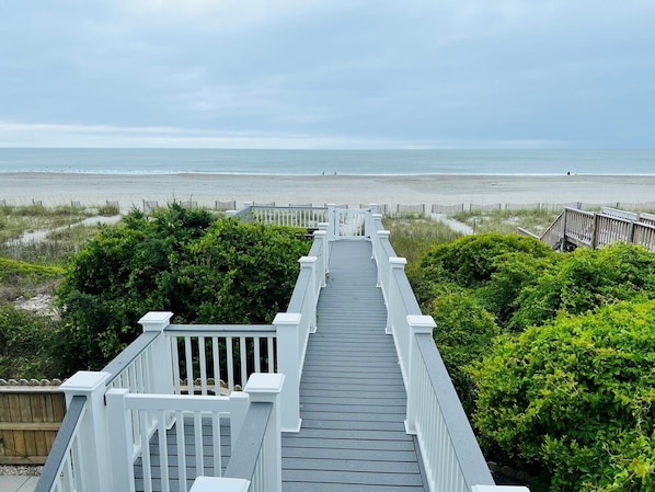 A wooden boardwalk leading to a beach with a view of the ocean.
