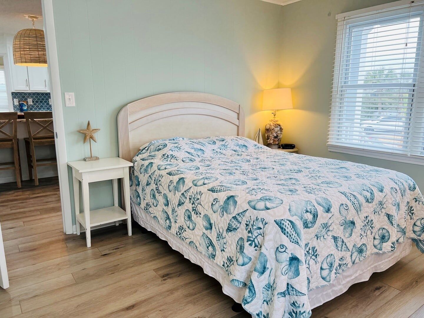 A bedroom with a bed, bedside table, lamp, and a window with blinds.