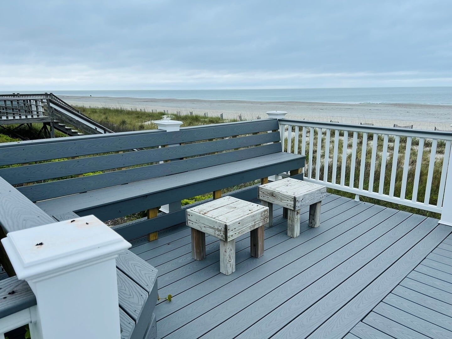 Een houten terras met een bank en twee stoelen, met uitzicht op een strand.