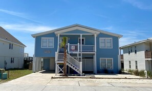 A two-story residential building with a balcony, a garage, and a small palm tree in the front yard. - Beach Time 5 Bedroom Home by RedAwning (Supply)