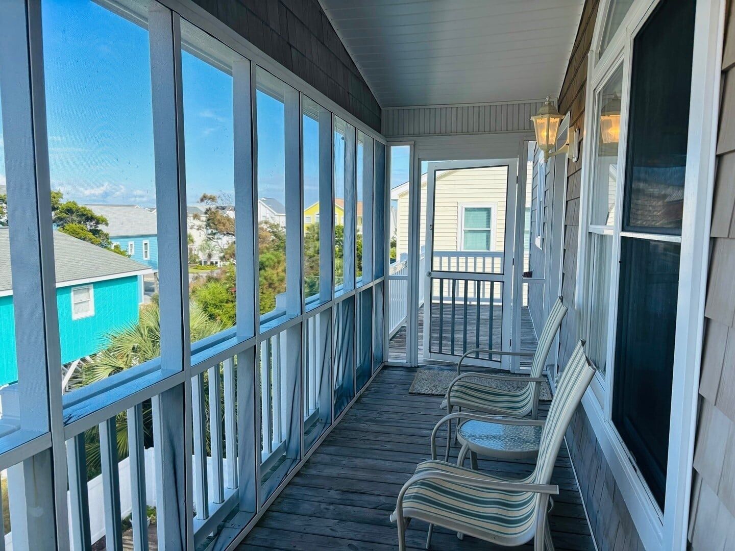 A covered porch with a view of the neighborhood, featuring a railing, a bench, and a table.