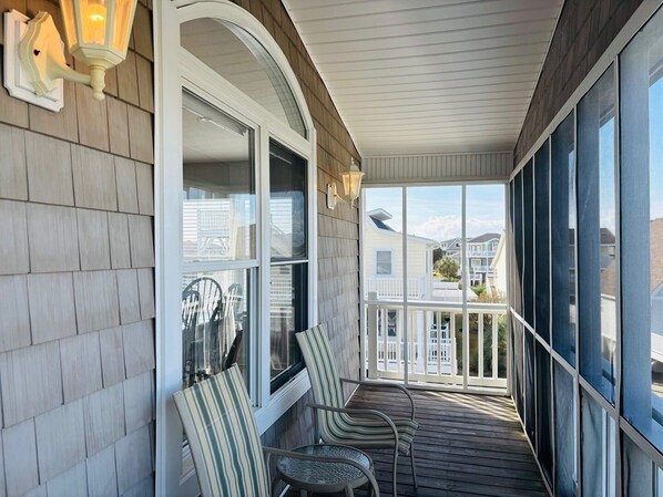 A covered porch with two chairs, a table, and a view of neighboring houses.