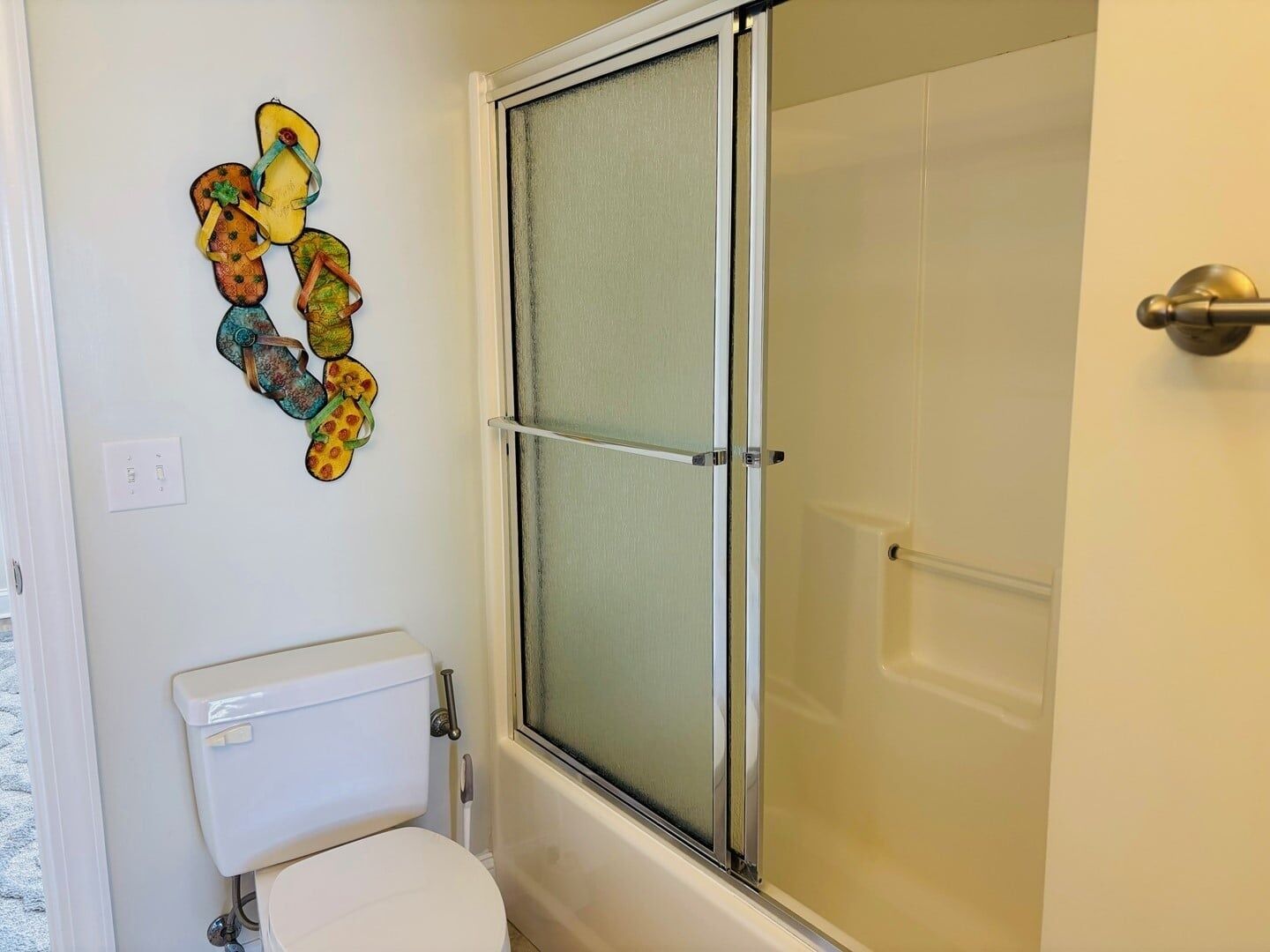 A bathroom with a toilet, a shower with a glass door, and a wall decoration.